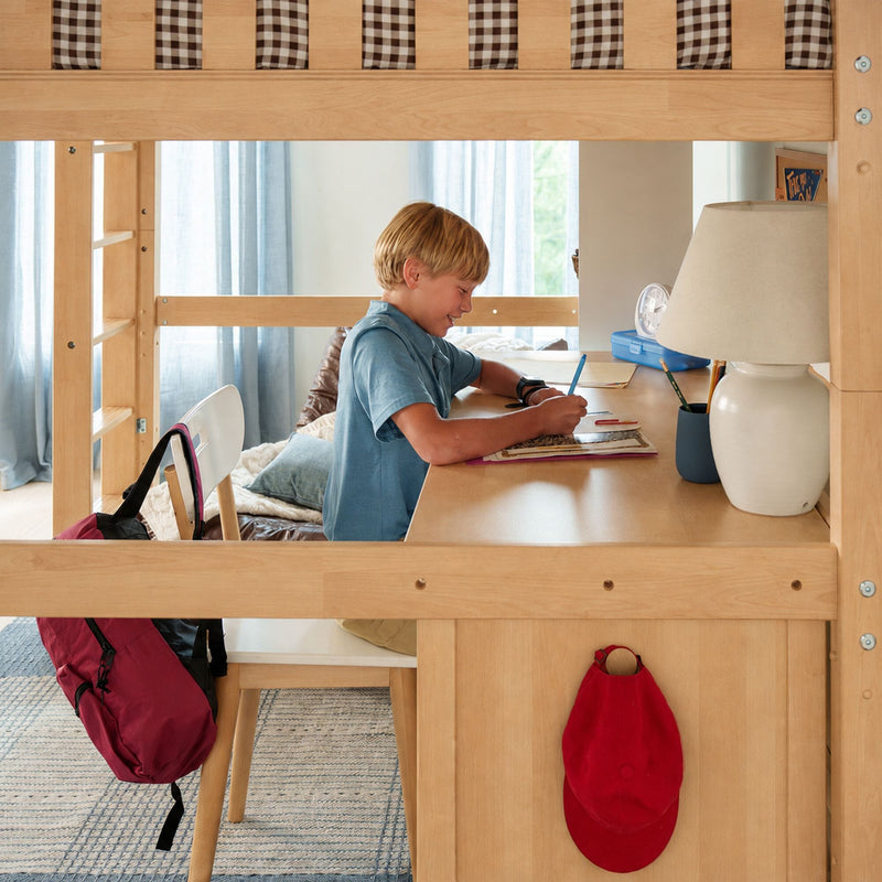 Child doing homework at a light-wood loft bunk bed with built-in study desk, lamp, backpack and school supplies in a bright kids' bedroom