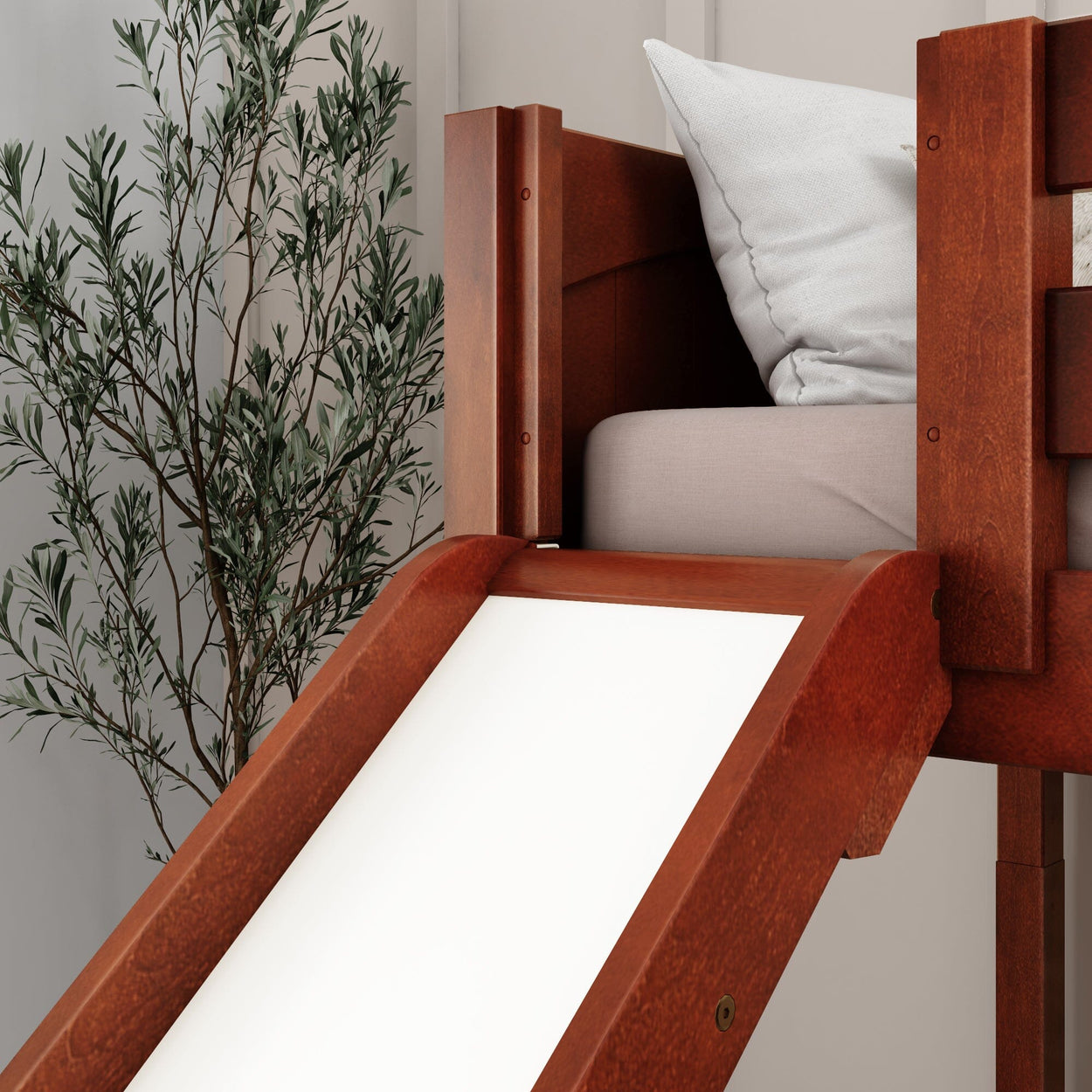 Wooden loft bed with slide and storage, featuring white cushion and indoor plant for modern children's bedroom decor.