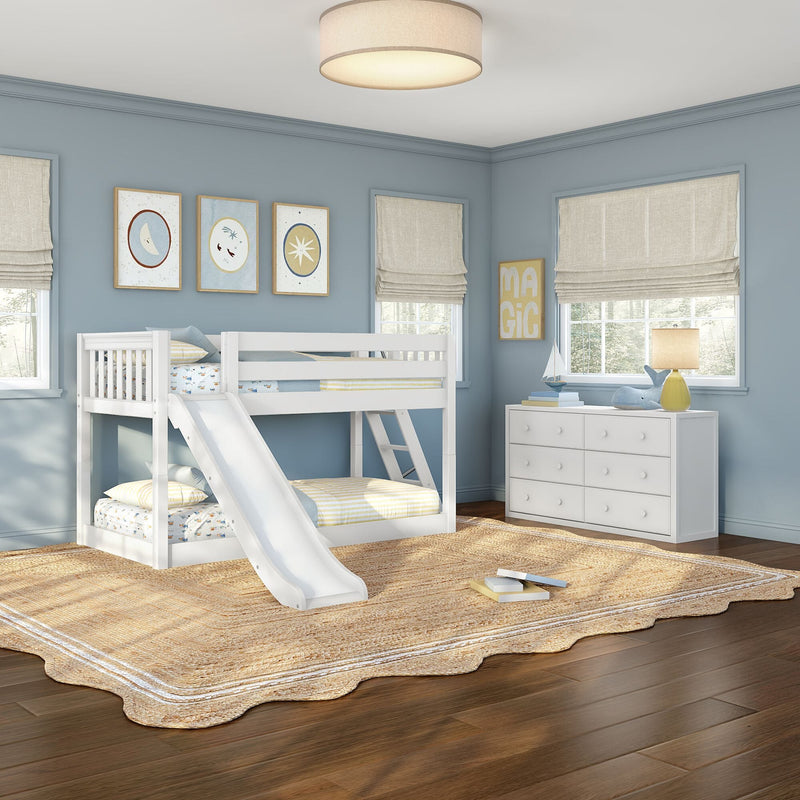 Kids bedroom with white bunk bed and slide, pale blue walls, beige woven jute rug, white dresser, sailboat toy and table lamp