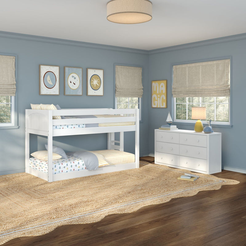 Children's coastal bedroom with white bunk bed, soft blue walls, framed nursery wall art, beige Roman shades, white dresser, yellow lamp and jute rug on hardwood floor