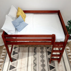 Cherry-finish solid wood loft bed with ladder, white sheets and blue and yellow pillows over a patterned boho rug — space-saving bedroom furniture