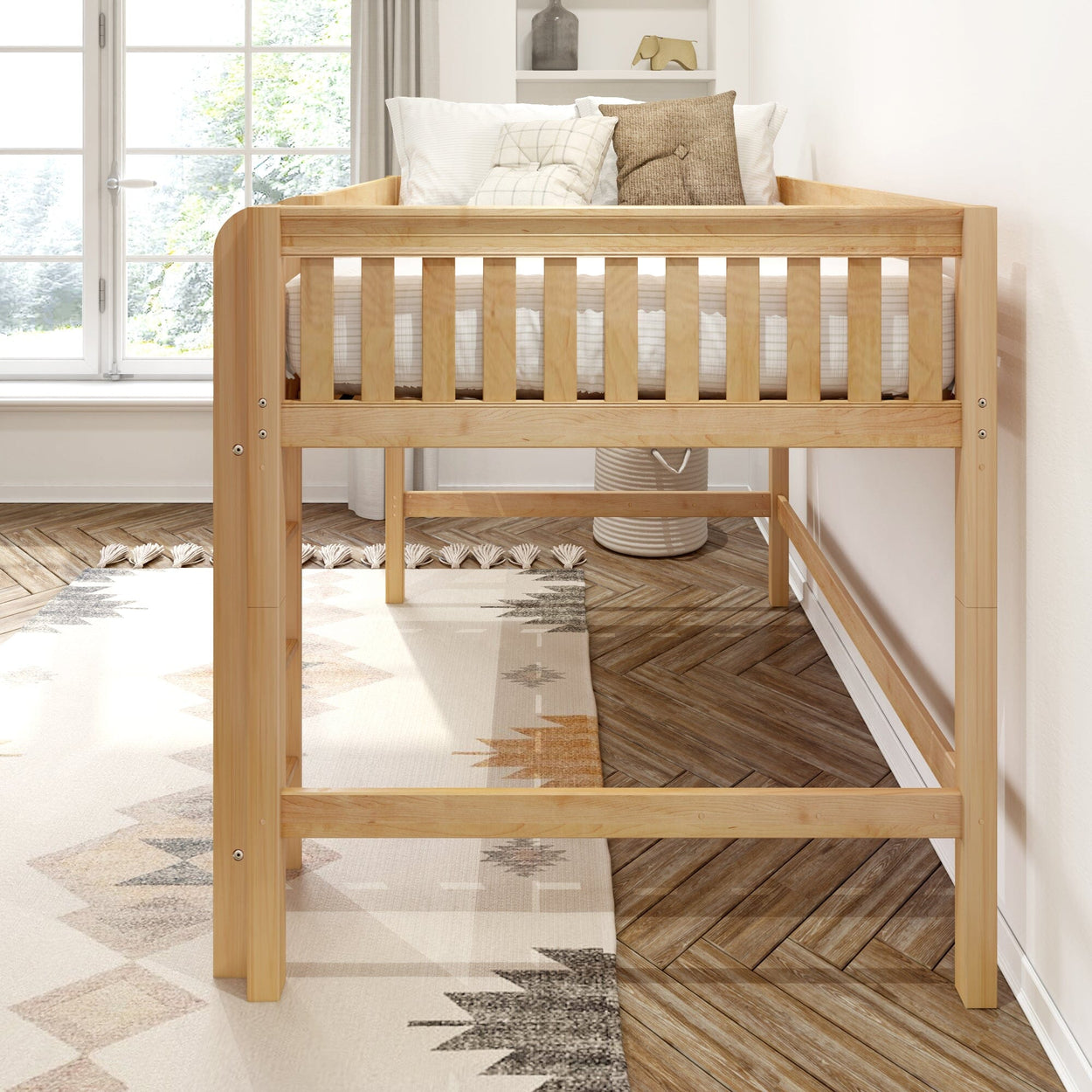Elevated natural wood toddler loft bed with slatted guardrail, white bedding and decorative pillows in bright modern nursery with herringbone hardwood floor and geometric rug