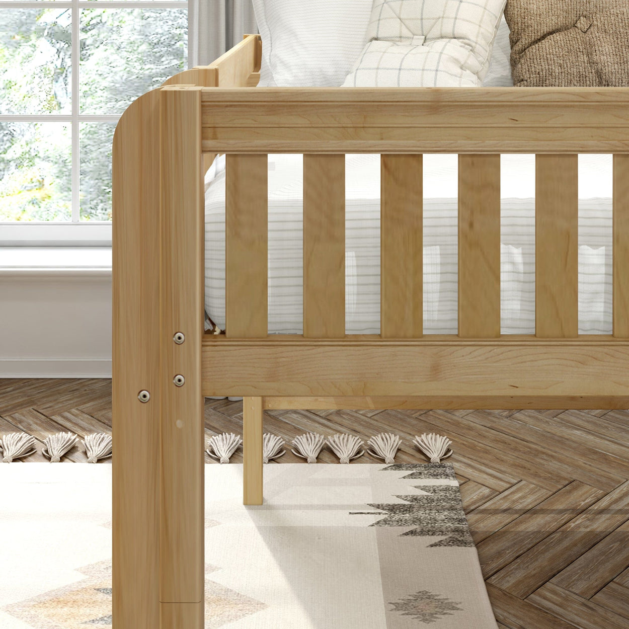 Natural solid wood slatted crib in bright nursery with white striped bedding, textured throw pillows, patterned area rug and herringbone wood floor