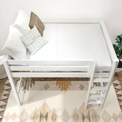 White wooden loft bed with ladder, white bedding and decorative pillows over geometric boho rug on hardwood floor with potted plant accent