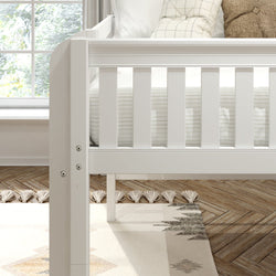 White wooden baby crib close-up in neutral modern nursery with striped bedding, textured pillows, boho tassel rug, and herringbone wood floor by sunlit window