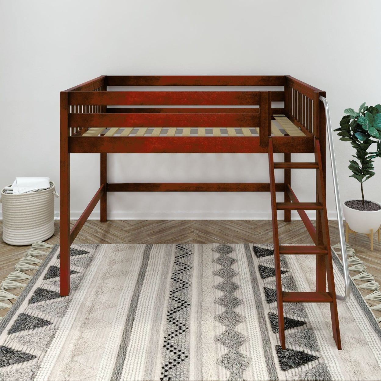 Rustic red-brown wooden loft bed with side ladder and slatted guardrails over a gray patterned area rug in a minimalist bedroom with a potted plant and woven laundry basket.