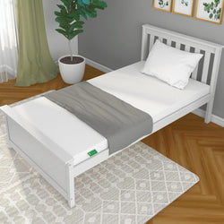 Single white bed with mattress, gray blanket, and pillow in a modern bedroom with wooden floor and plant.