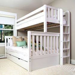 White wooden bunk bed with trundle drawer and built-in ladder in a modern children's bedroom with white bedding and decorative pillows