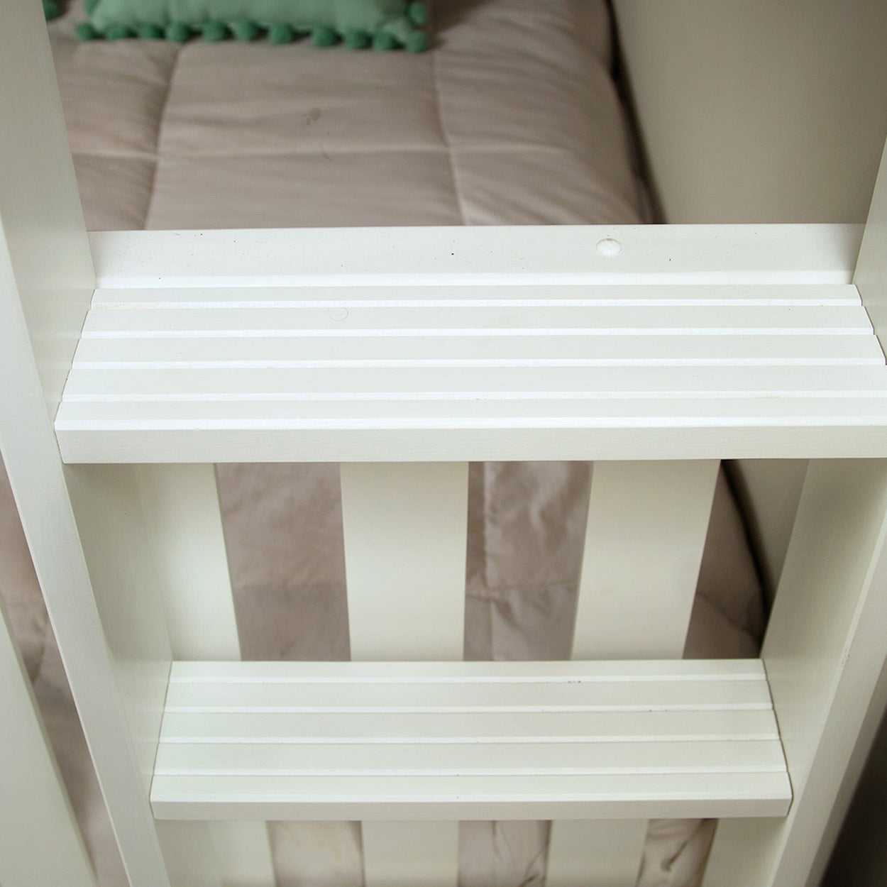 Close-up of a white painted wooden bunk bed ladder with horizontal slatted rungs in a bedroom