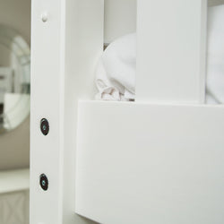 Close-up of white wooden bunk bed frame showing metal bolt hardware, mattress rail and folded white bedding.