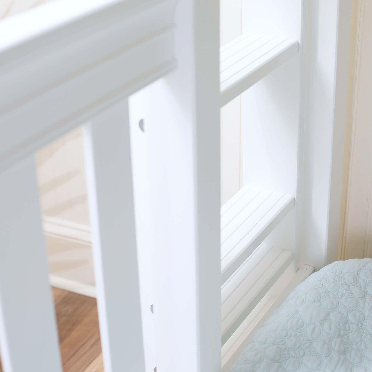 White wooden ladder attached to bunk bed with light blue quilt.