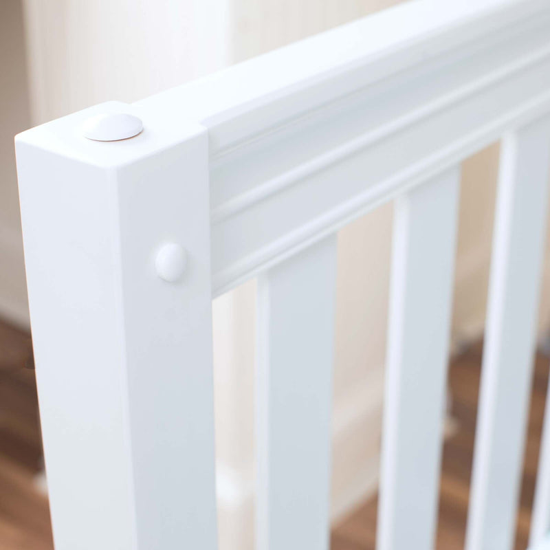 Close-up of white wooden baby crib rail with rounded post cap and vertical slats, nursery furniture detail