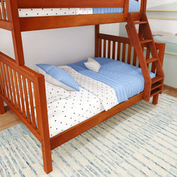 Wooden bunk bed with blue and white bedding and stairs, placed on a patterned rug in a bright room.