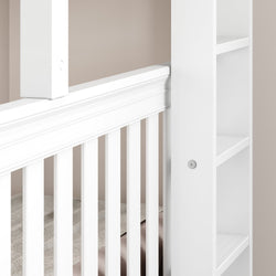 White baby crib with elegant side rails and built-in storage shelves against a beige wall.
