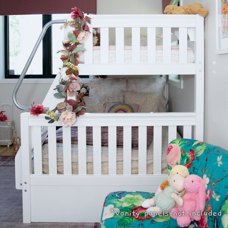 White wooden twin-over-full bunk bed with floral garland, pastel bedding and rainbow pillow in a styled kids' bedroom with plush toys on a floral chair
