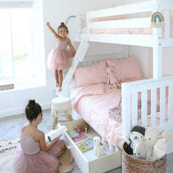 Two young girls playing in a charming pink-themed girl's bedroom with a white bunk bed and plush toys.