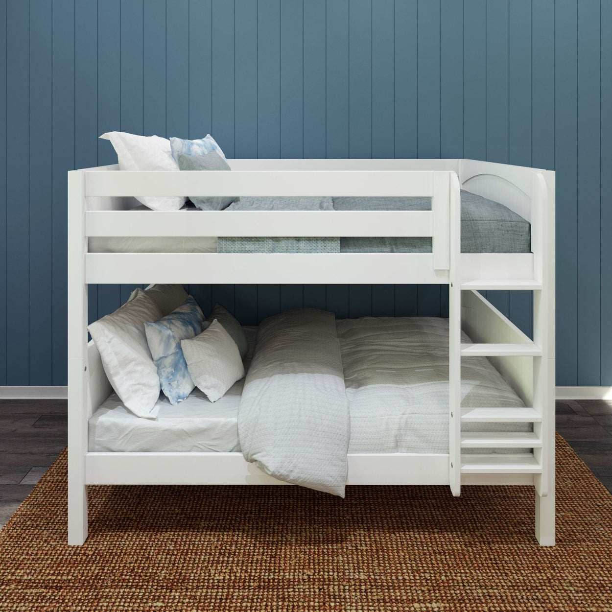 White wooden bunk bed with comfortable pillows and bedding in a modern bedroom with blue paneled wall and brown carpet.