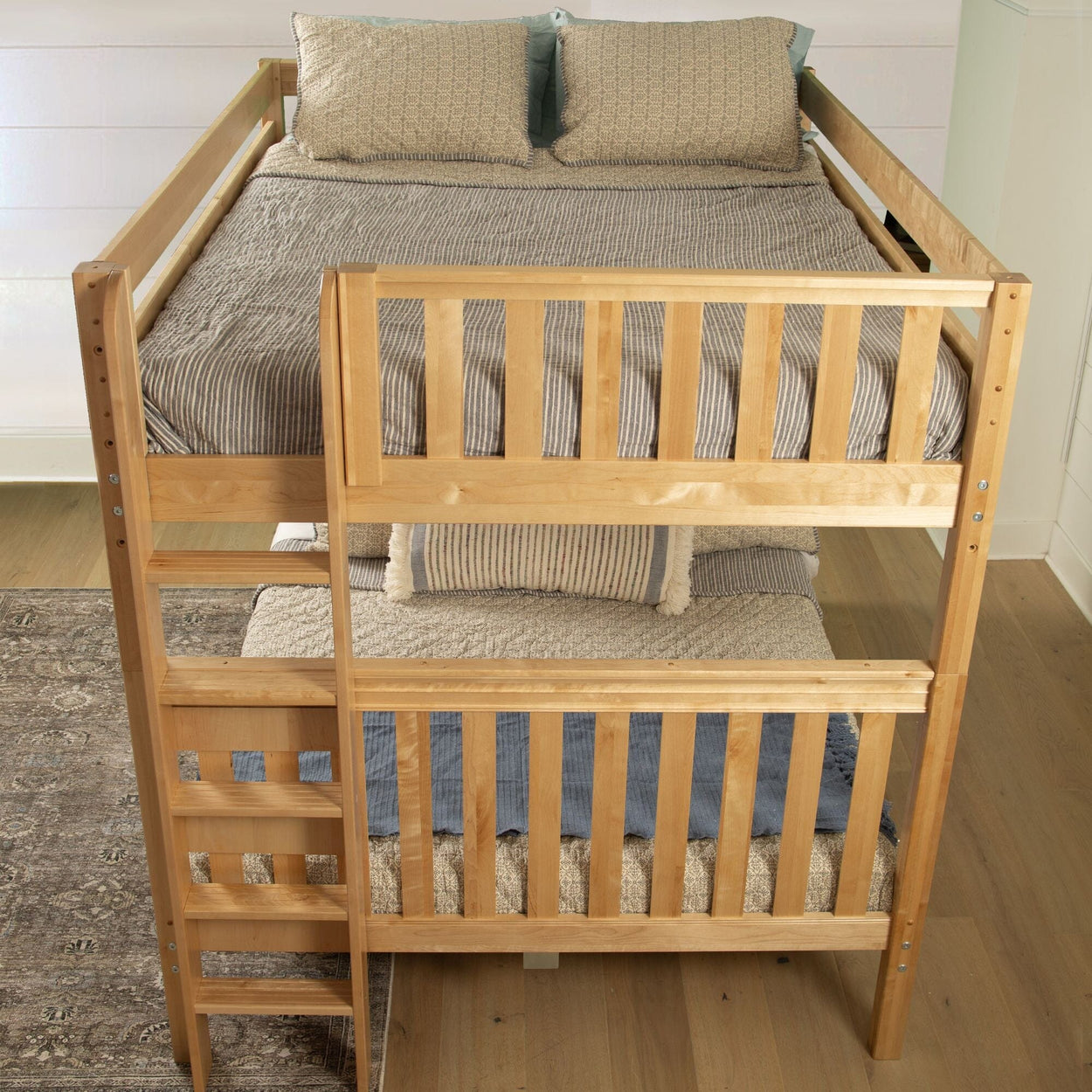 Wooden twin over full bunk bed with striped bedding in a cozy bedroom setting.
