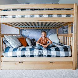 Child sitting on a wooden bunk bed with blue plaid bedding and decorative pillows in a cozy bedroom.