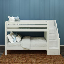 White wooden bunk bed with stairs and bedding against a blue paneled wall.