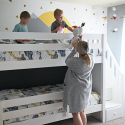 Children playing on a white bunk bed while a woman gives them a stuffed toy.
