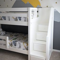 White bunk bed with built-in storage stairs in a kids' room with decorative wall art.