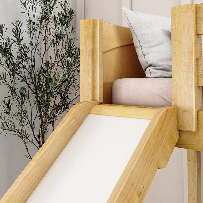 Wooden indoor kids' bed slide in natural pine with soft pink mattress and white pillow next to a leafy indoor plant, modern neutral nursery decor