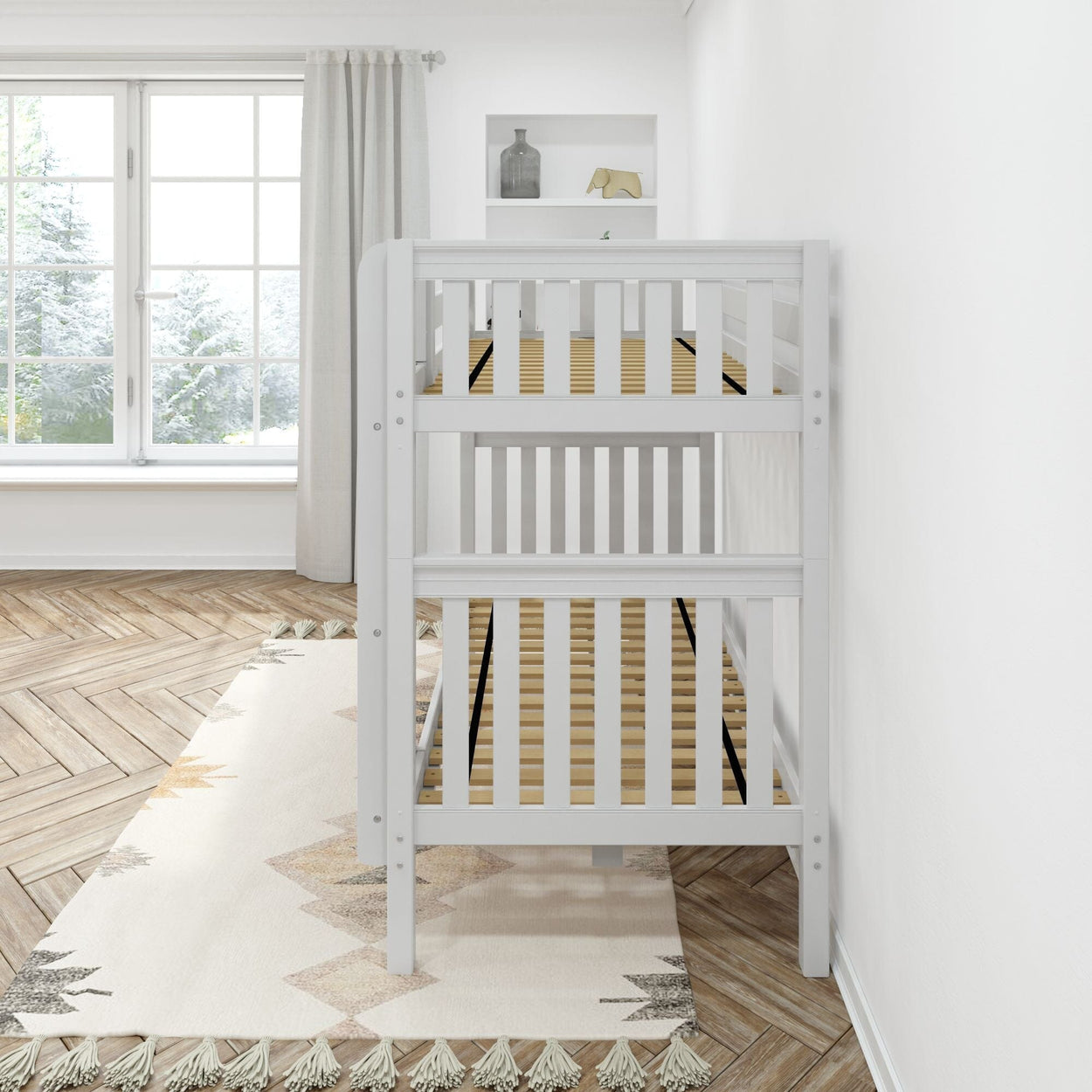 White wooden baby crib in a bright nursery room with herringbone wood floors and a large window.