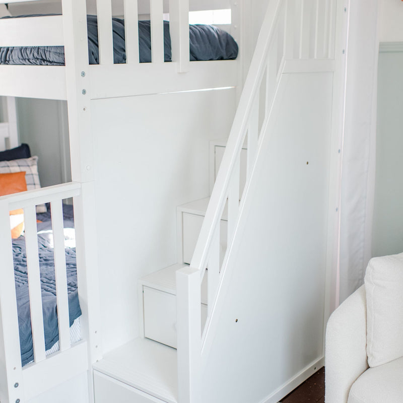 White wooden bunk bed with built-in storage stairs and navy bedding in a bright modern kids' bedroom