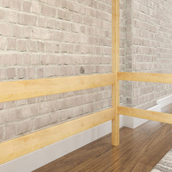 Wooden bed frame against exposed brick wall on hardwood flooring.