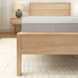 Contemporary wooden bed frame with plush mattress in a minimalist bedroom setting.
