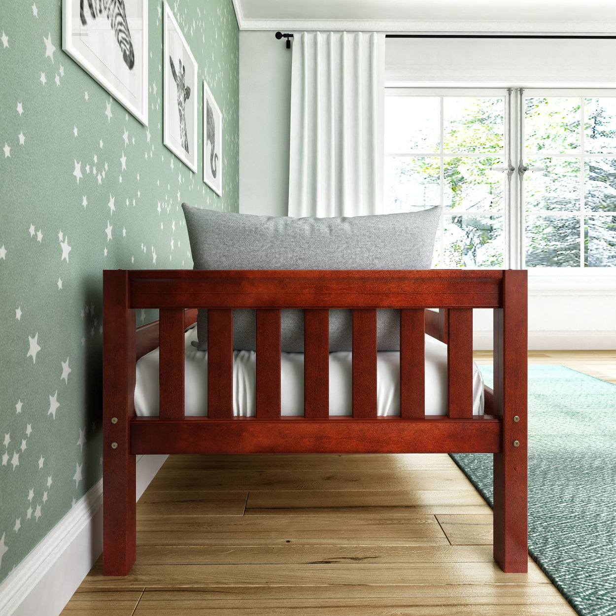 Wooden toddler bed with gray pillow in star-themed nursery room with green walls and natural light.