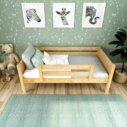 Toddler bed in a stylish nursery with wooden frame, giraffe and zebra wall art, and teddy bear.