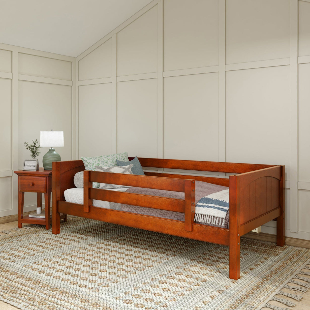 Wooden daybed with guardrail and decorative pillows in a cozy bedroom setting with a bedside table and lamp.