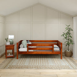 Wooden daybed with side rails in a cozy, modern bedroom featuring a potted plant and a bedside table with a lamp on a patterned rug.