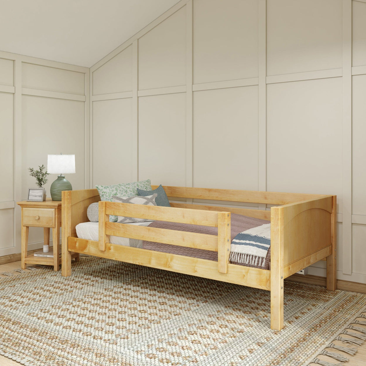 Wooden toddler bed with guardrails in a cozy bedroom setting featuring a nightstand and decorative lamp.