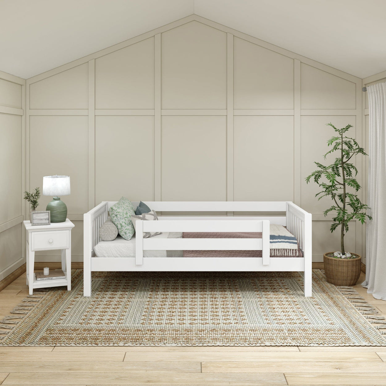 Modern minimalist bedroom with white daybed, cozy pillows, side table with lamp, and indoor plant on patterned rug.