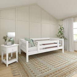White toddler daybed in a cozy bedroom with patterned rug, nightstand, and indoor plant.