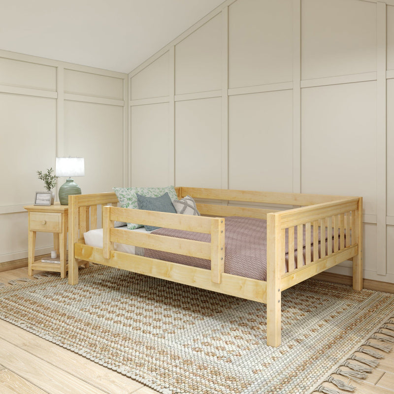 Natural wood toddler bed in a modern nursery with pastel throw pillows, bedside lamp on a nightstand, textured woven rug and beige paneled walls