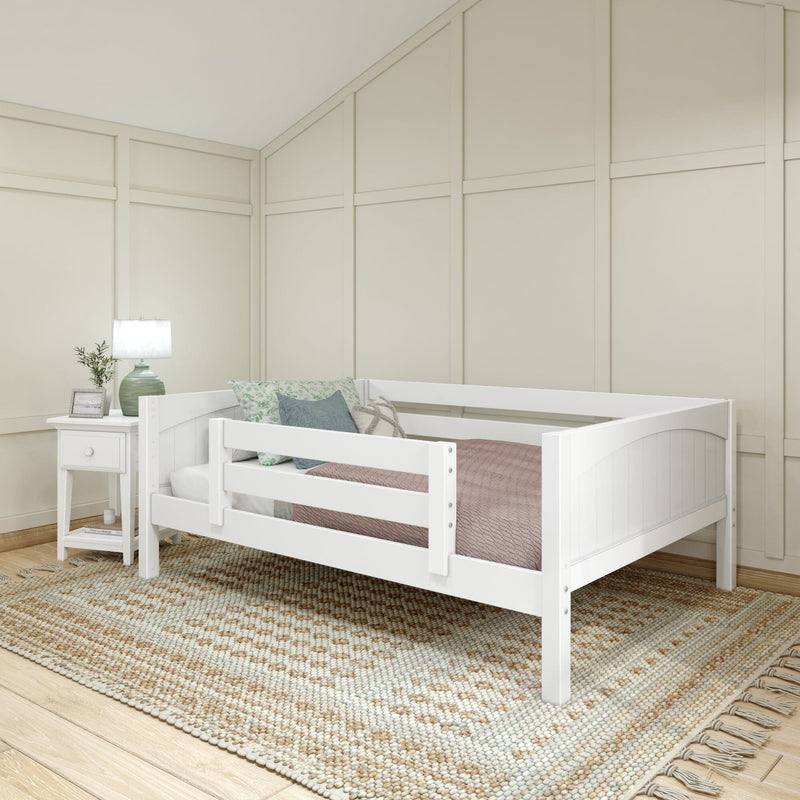 White toddler bed in neutral nursery with beige board-and-batten walls, green bedside lamp, patterned pillows and woven textured rug