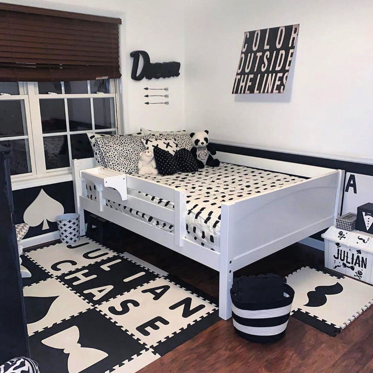 Monochrome toddler bedroom with white bed, polka dot pillows, panda toys, and alphabet-themed decor.