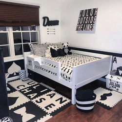 Monochrome toddler bedroom with white bed, polka dot pillows, panda toys, and alphabet-themed decor.