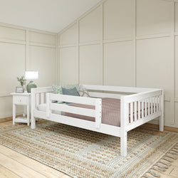 White toddler bed with pink bedding in a cozy room with a bedside table and decorative pillows.