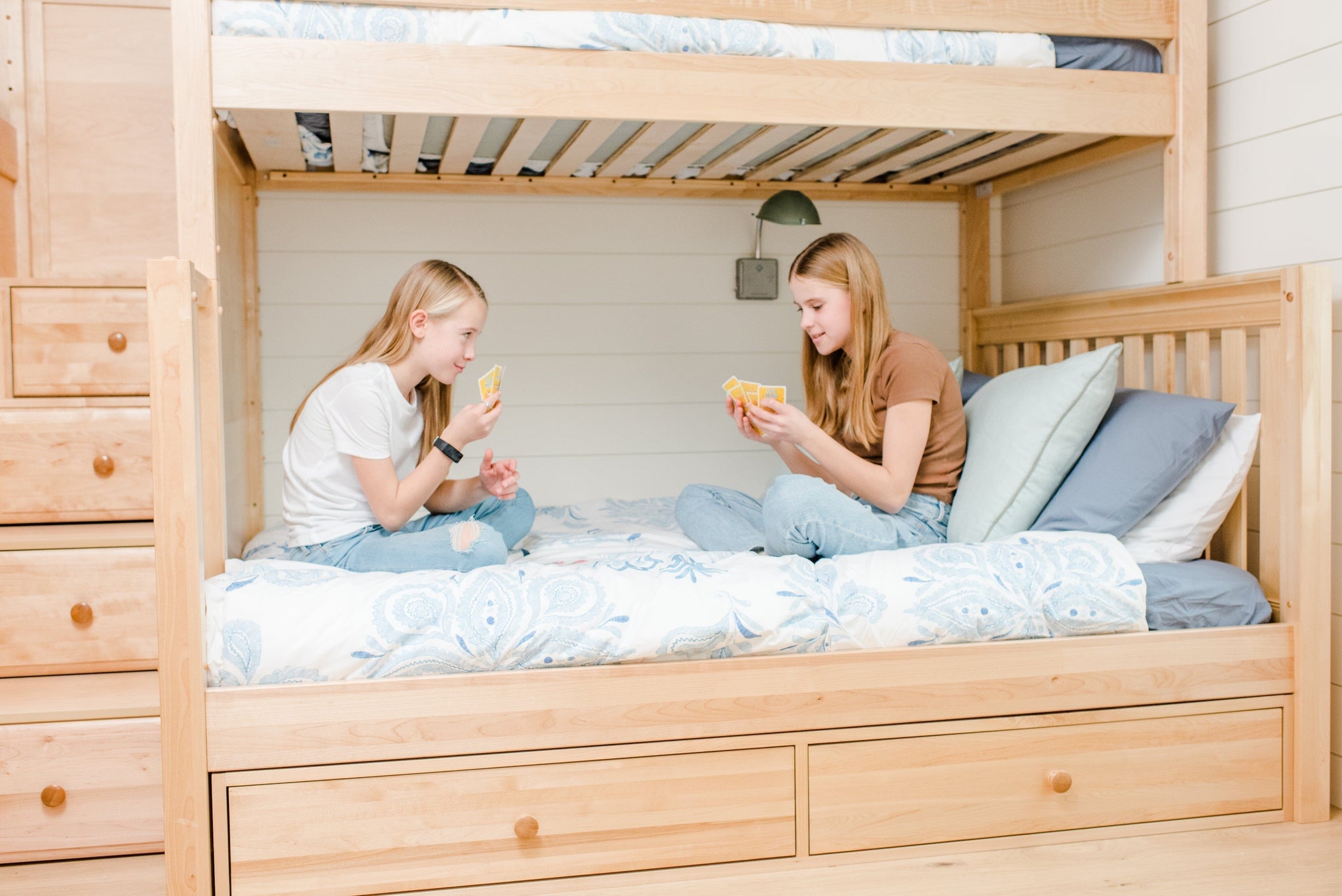 Quad bunk bed with stairs and storage drawers with two girls playing cards on bottom bunk 