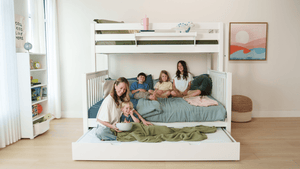 Mom and children relaxing on a white bunk bed with trundle and green bedding in a bright kids' bedroom