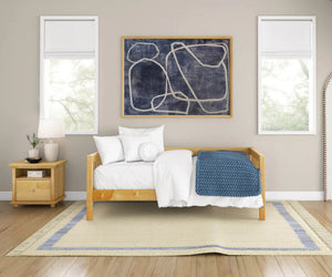 Daybed with white bedding in a room with art on the wall and a nightstand.