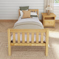 Cozy neutral farmhouse bedroom with twin wooden bed, woven throw pillow and green linen cushions, wooden nightstand and pleated lamp against white shiplap wall