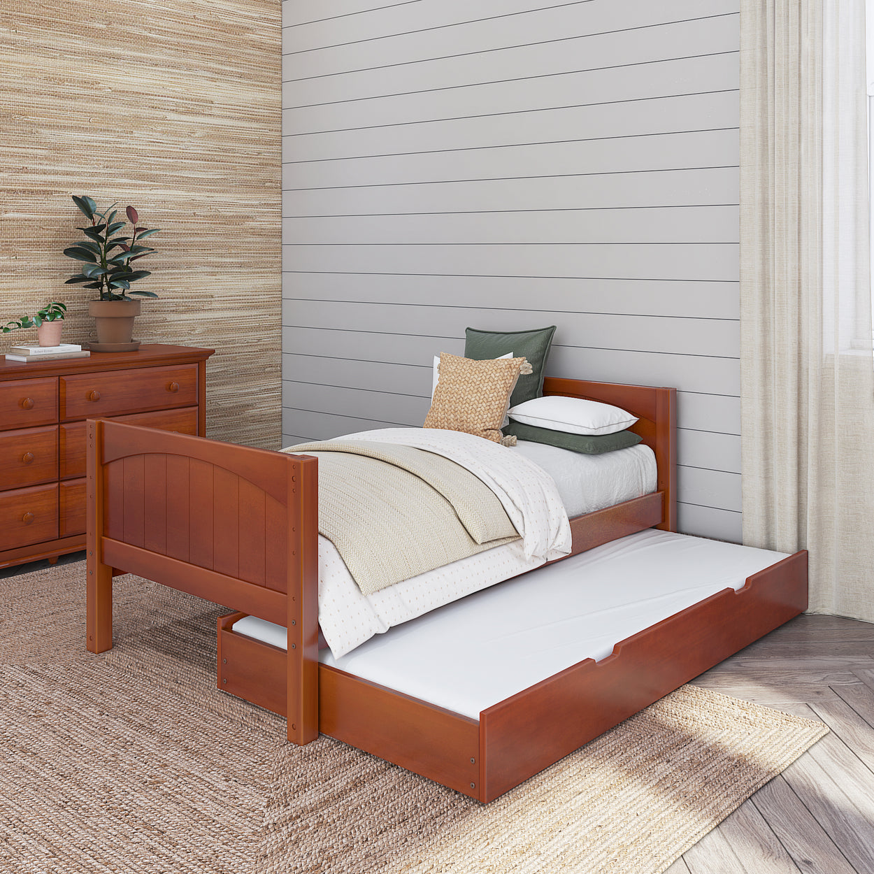 Wooden twin bed with trundle in bright bedroom featuring cozy bedding, dresser, and potted plant.