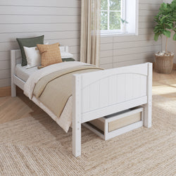 Single white wooden bed with olive and beige bedding in a cozy bedroom featuring a large window, potted plant, and light wood flooring.