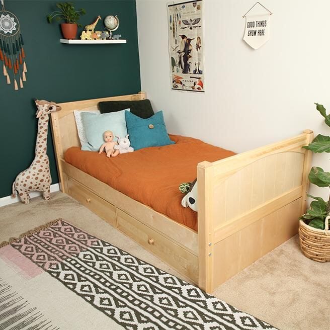 Kids bedroom wooden daybed with under-bed storage drawers, rust-orange bedding and teal pillows, green accent wall, plush giraffe toy and patterned boho rug